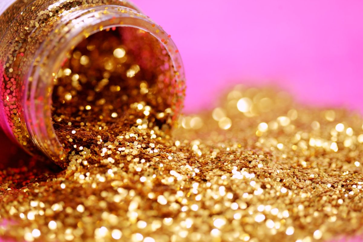A jar of gold glitter spilling out on a pink table.
