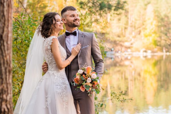 A newly wedded couple standing in front of a lake.